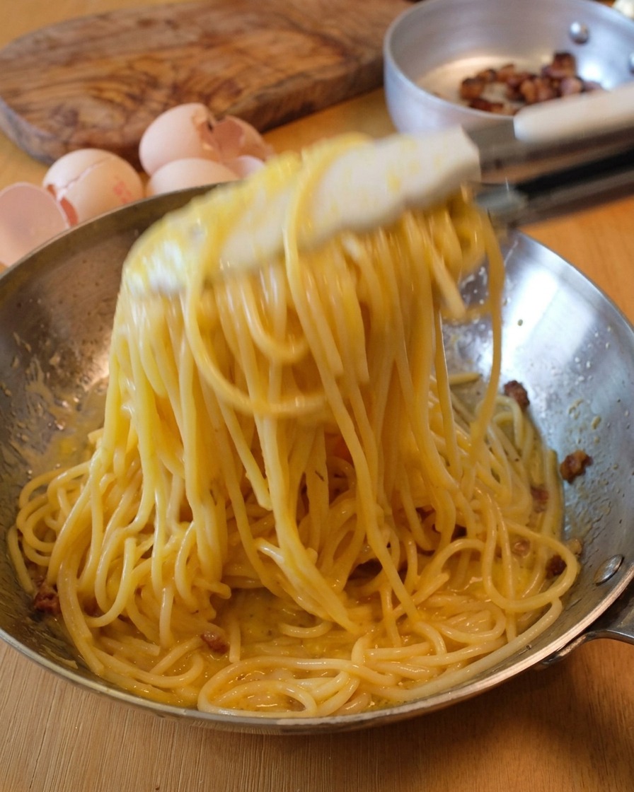 Mélange énergique des spaghettis avec une pince pour créer lémulsion de la carbonara.