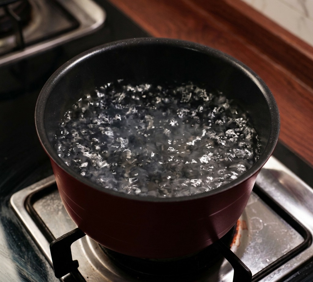 Une grande casserole rouge sur une cuisinière à gaz remplie deau bouillante avec de la vapeur.