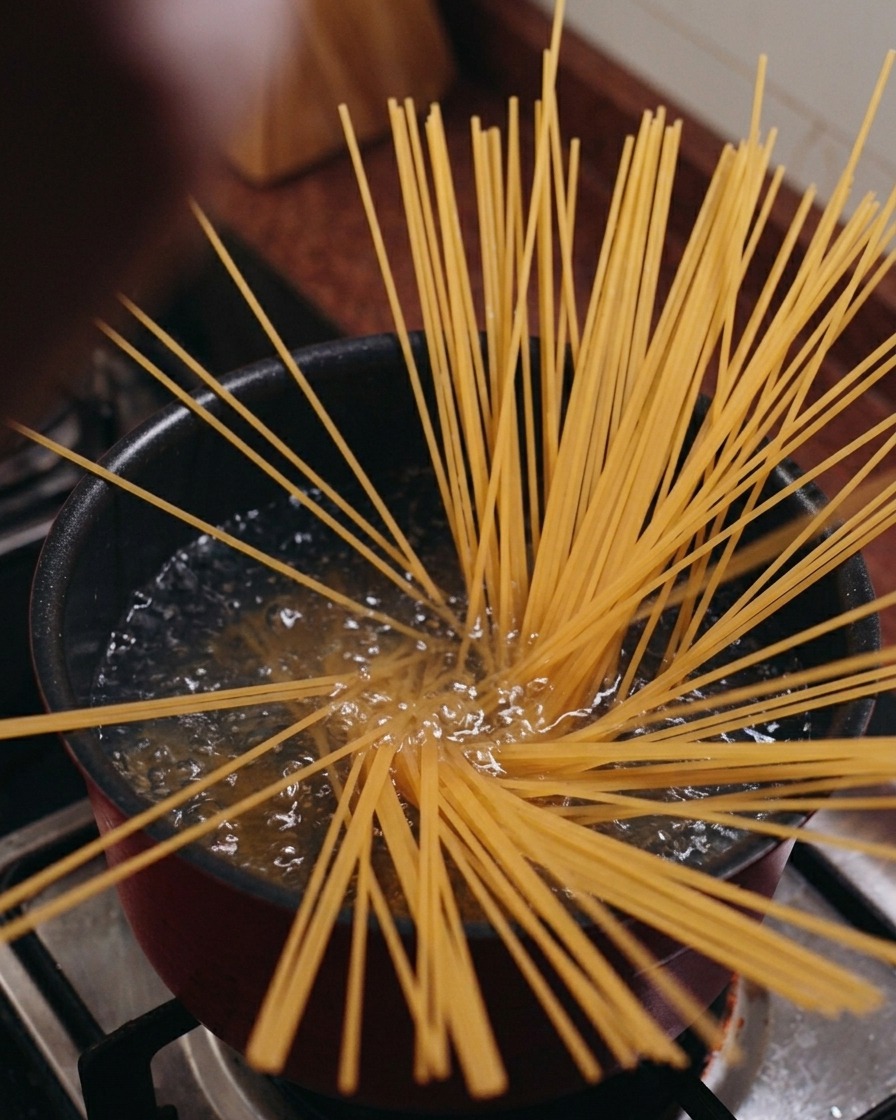 Des spaghetti secs posés verticalement dans une casserole deau bouillante, sévasant en étoile.