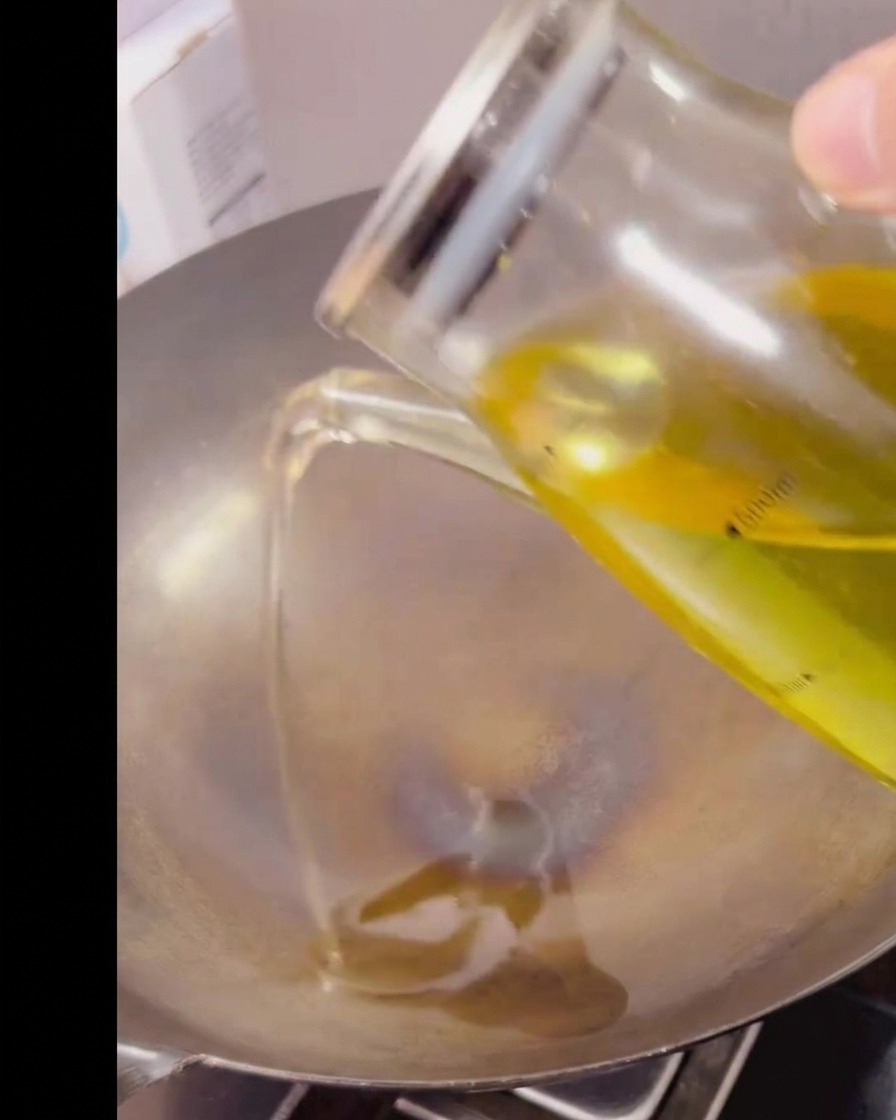 Huile de cuisson transparente versée depuis un pichet doseur en verre dans un wok en métal chaud et vide.