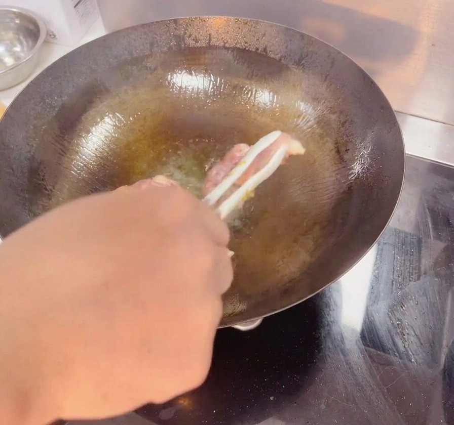 Une pince retourne une cuisse de poulet dans un wok sombre, révélant une peau dorée et croustillante.
