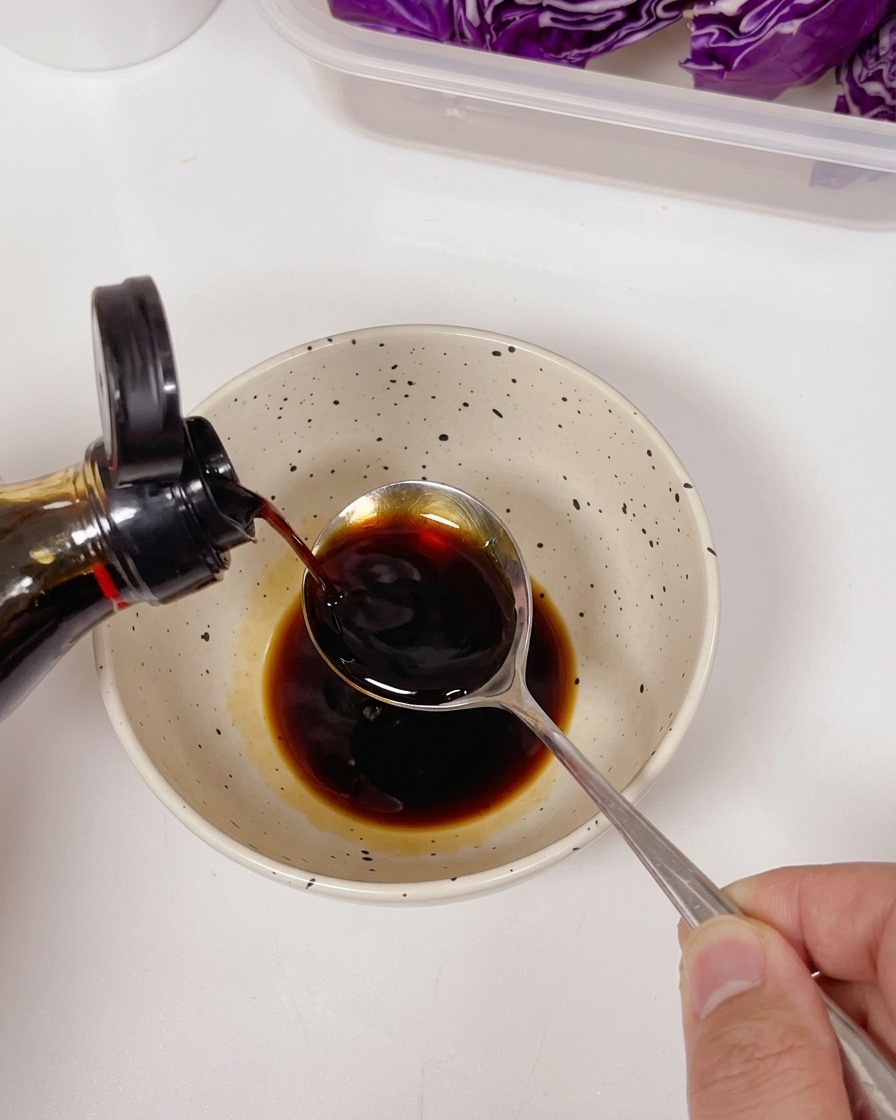 De la sauce soja claire versée dune bouteille dans une cuillère, au-dessus dun bol contenant une sauce foncée et des assaisonnements.