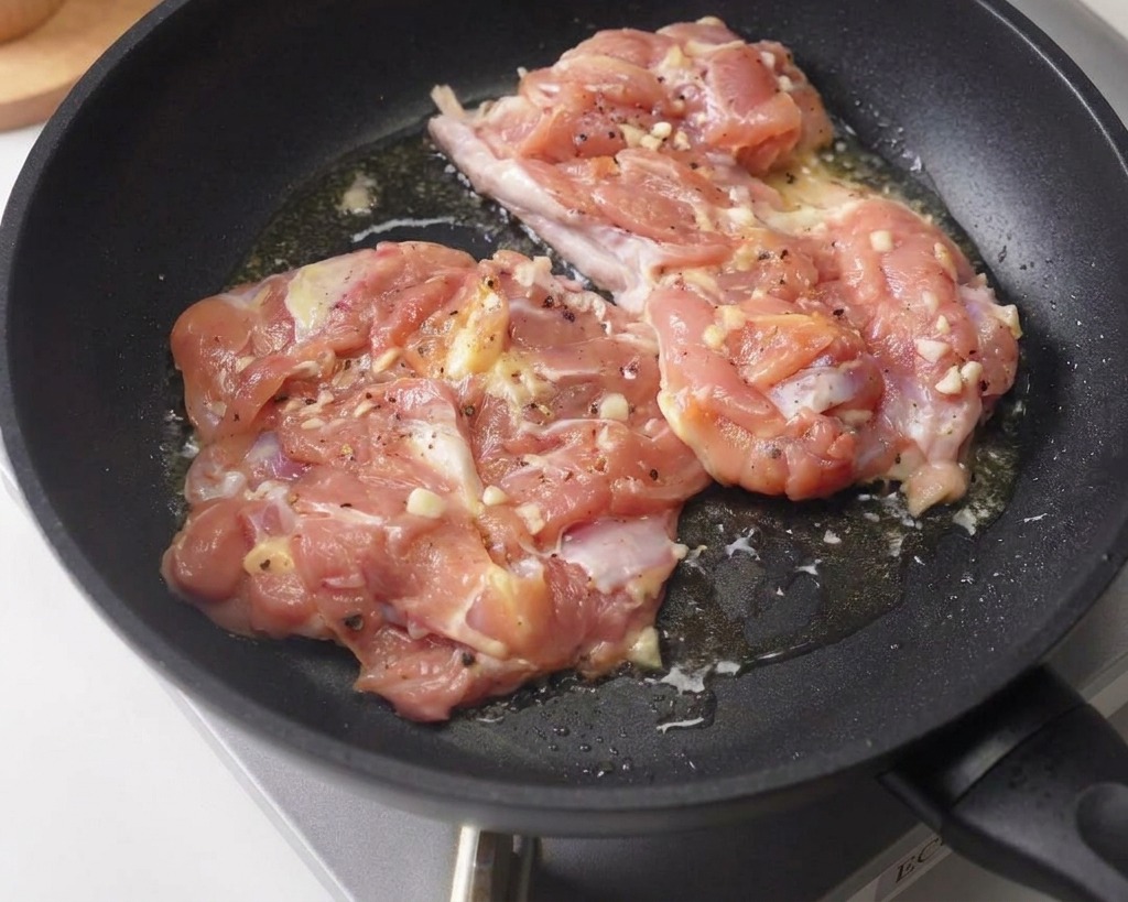 Deux hauts de cuisse de poulet marinés saisis côté peau dans une poêle antiadhésive bien chaude.