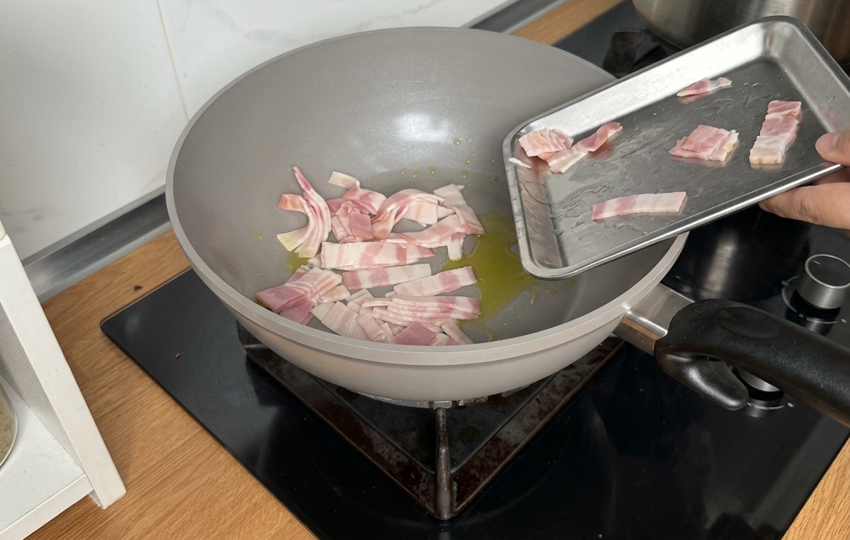 Verser des lanières de bacon cru dans une poêle grise contenant un filet dhuile dolive.