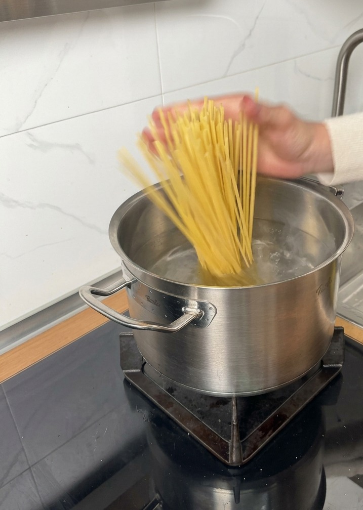 Des pâtes sèches ajoutées dans une casserole deau bouillante sur une plaque à induction.