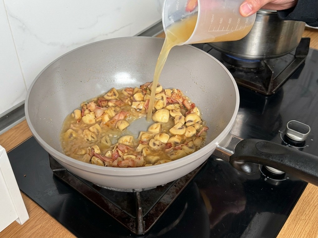 Bouillon de poulet versé depuis un verre doseur sur le mélange champignons et bacon.