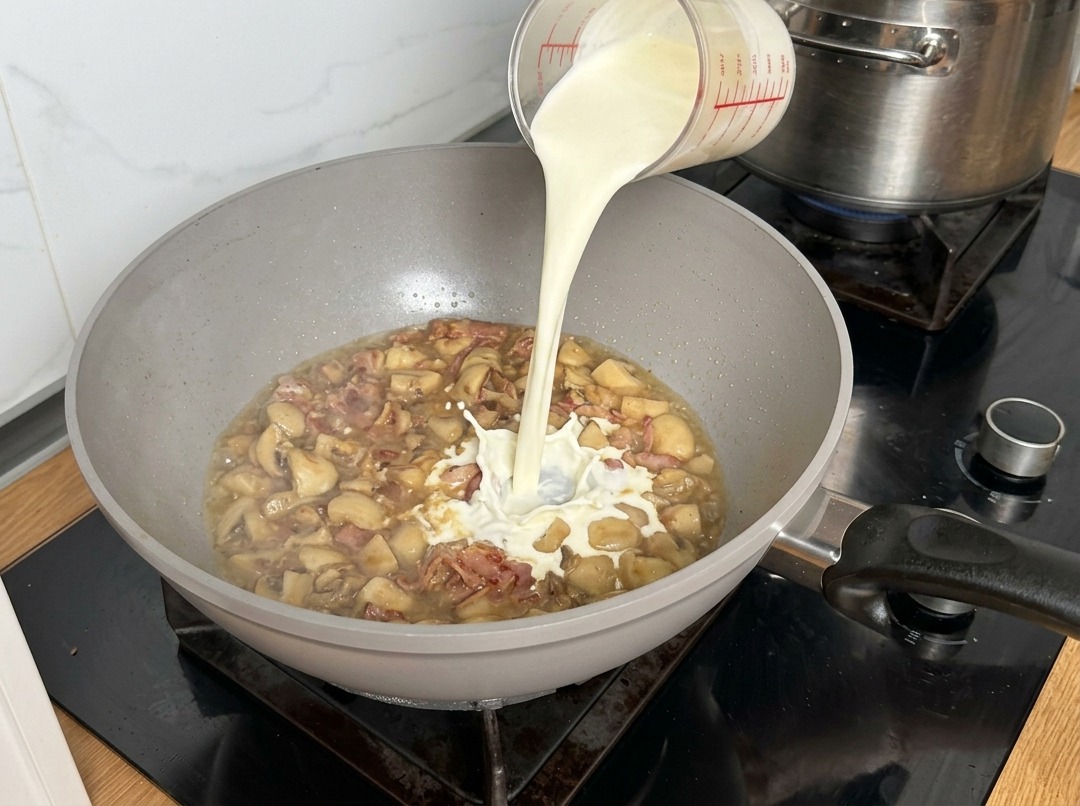 Crème liquide versée dans la poêle, créant un remous au contact de la base de champignons fumante.