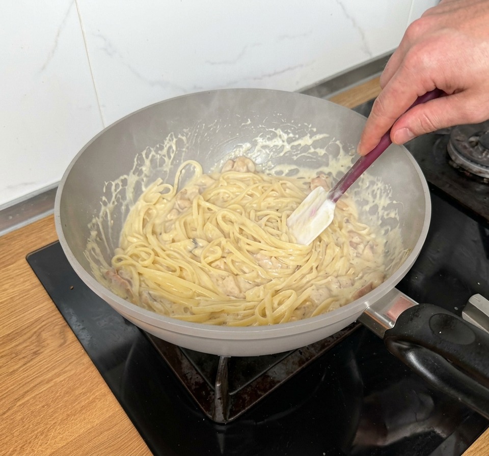 Mélange vigoureux de linguines dans une poêle remplie dune sauce riche, de bacon et de quartiers de champignons.