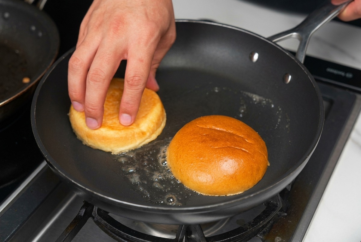 Demi-pains à burger toastés face vers le bas dans une poêle avec du beurre fondu crépitant.