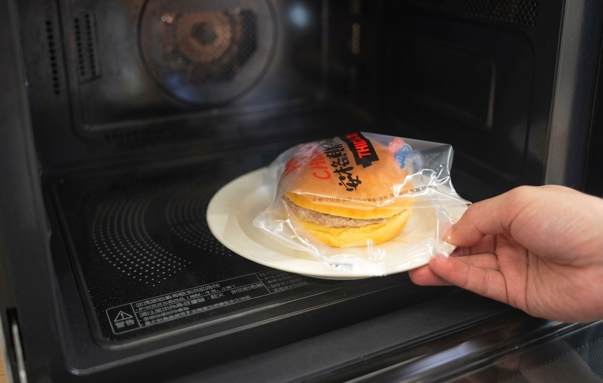 Une main plaçant la partie supérieure dun pain brioché toasté sur un burger garni doignons et de fromage fondu.