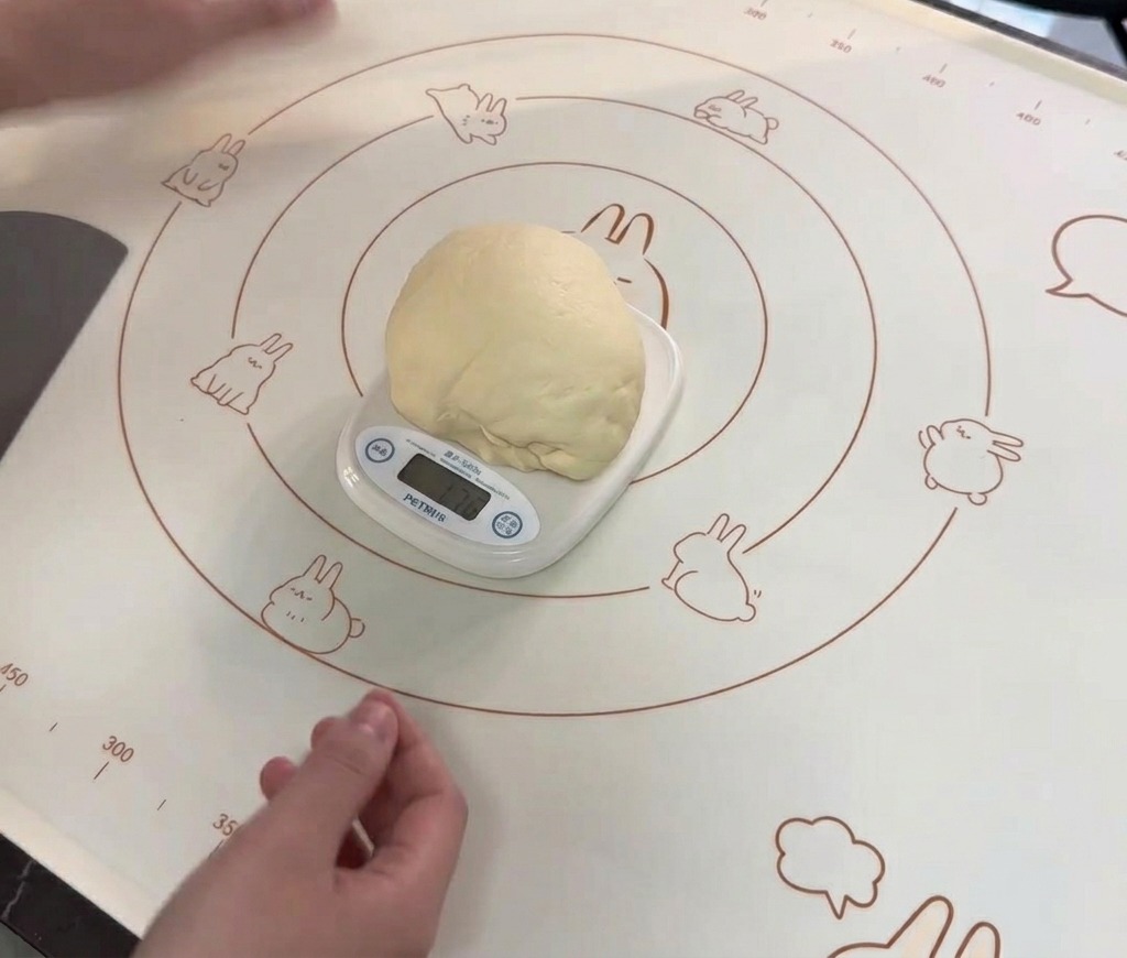 Une grosse boule de pâte bien lisse posée sur une balance de cuisine numérique blanche sur un tapis de cuisson.