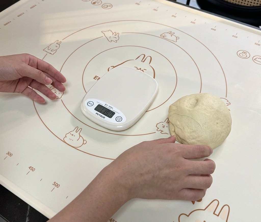 Un petit pâton reposant sur un tapis de cuisson à côté dune balance numérique affichant son poids.
