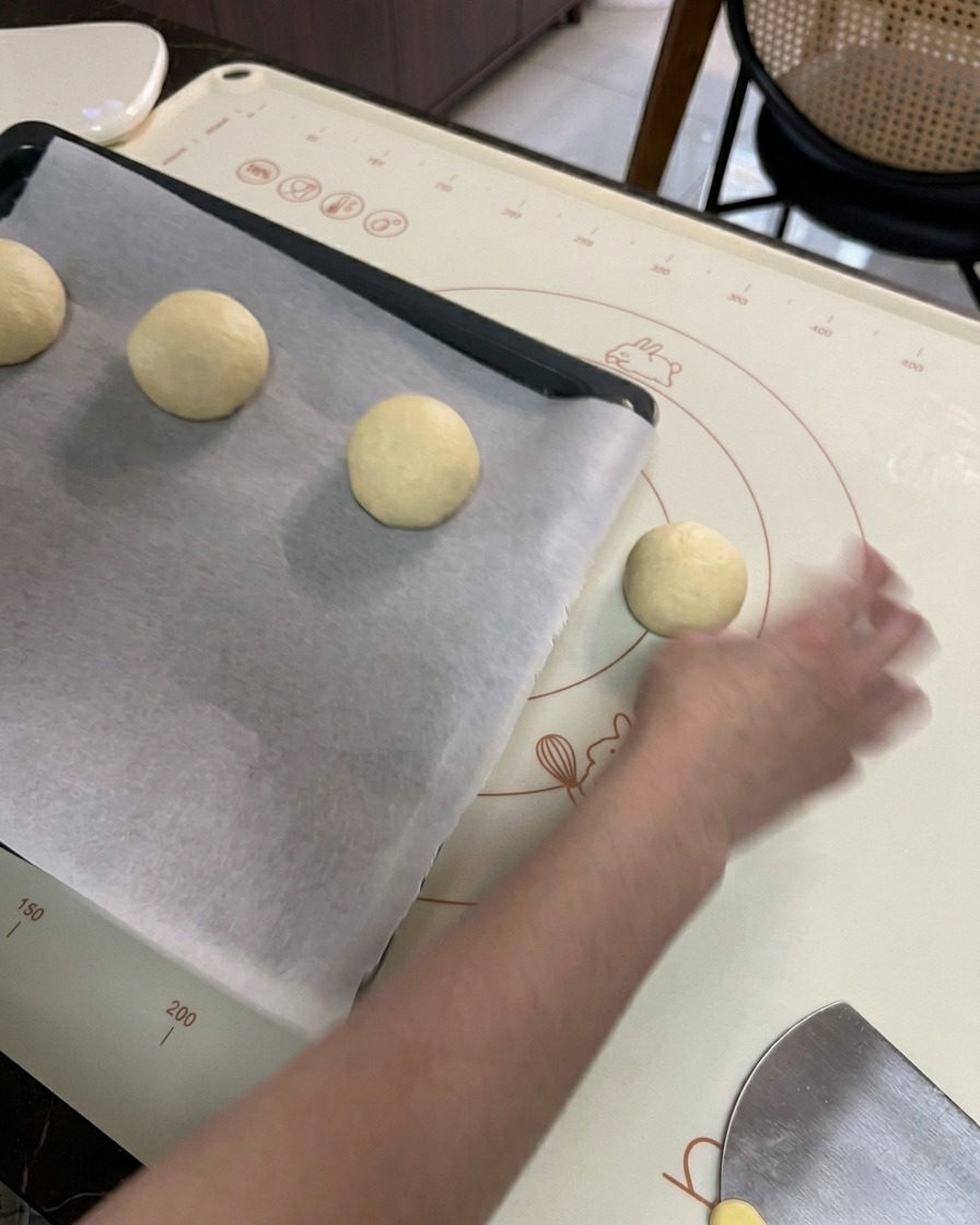 Une main plaçant les boules de pâte façonnées sur une plaque de cuisson recouverte de papier sulfurisé blanc.