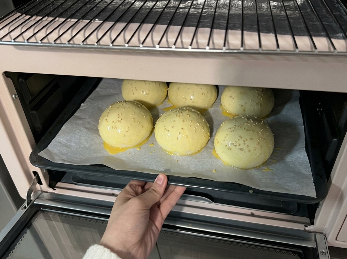Une plaque de pâtons recouverts de sésame insérée dans un petit four rose pour la cuisson.
