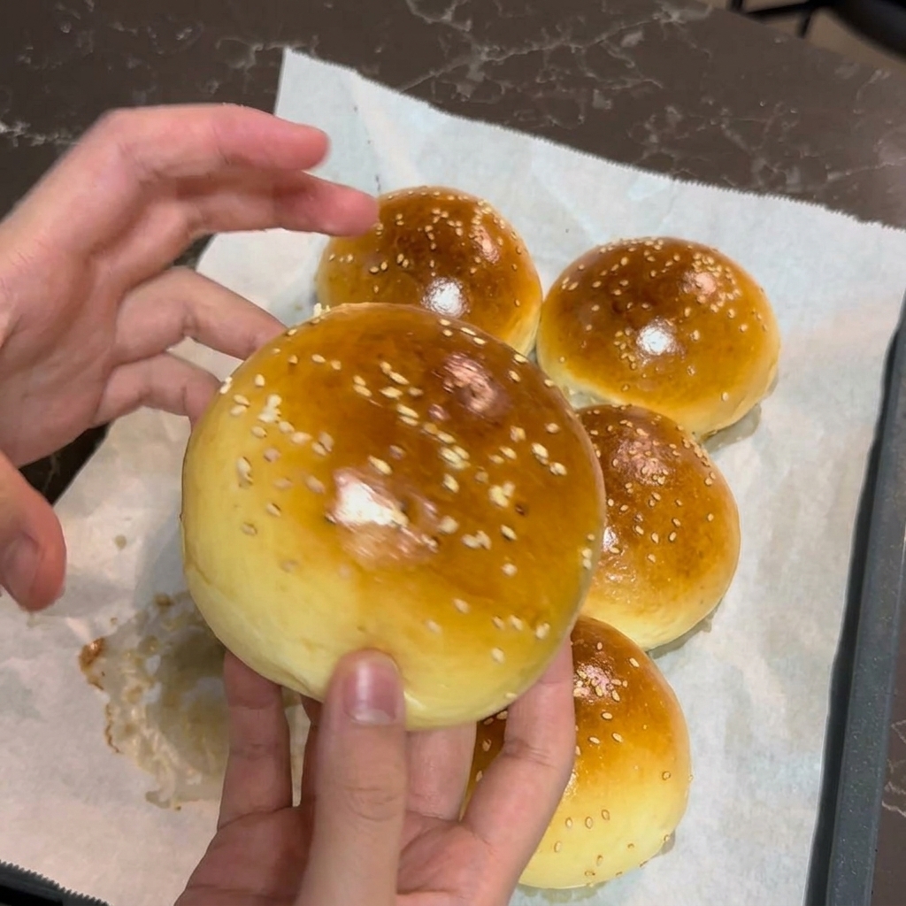 Les mains dune personne tenant délicatement un pain à burger tout juste cuit, doré à souhait et parsemé de sésame blanc.