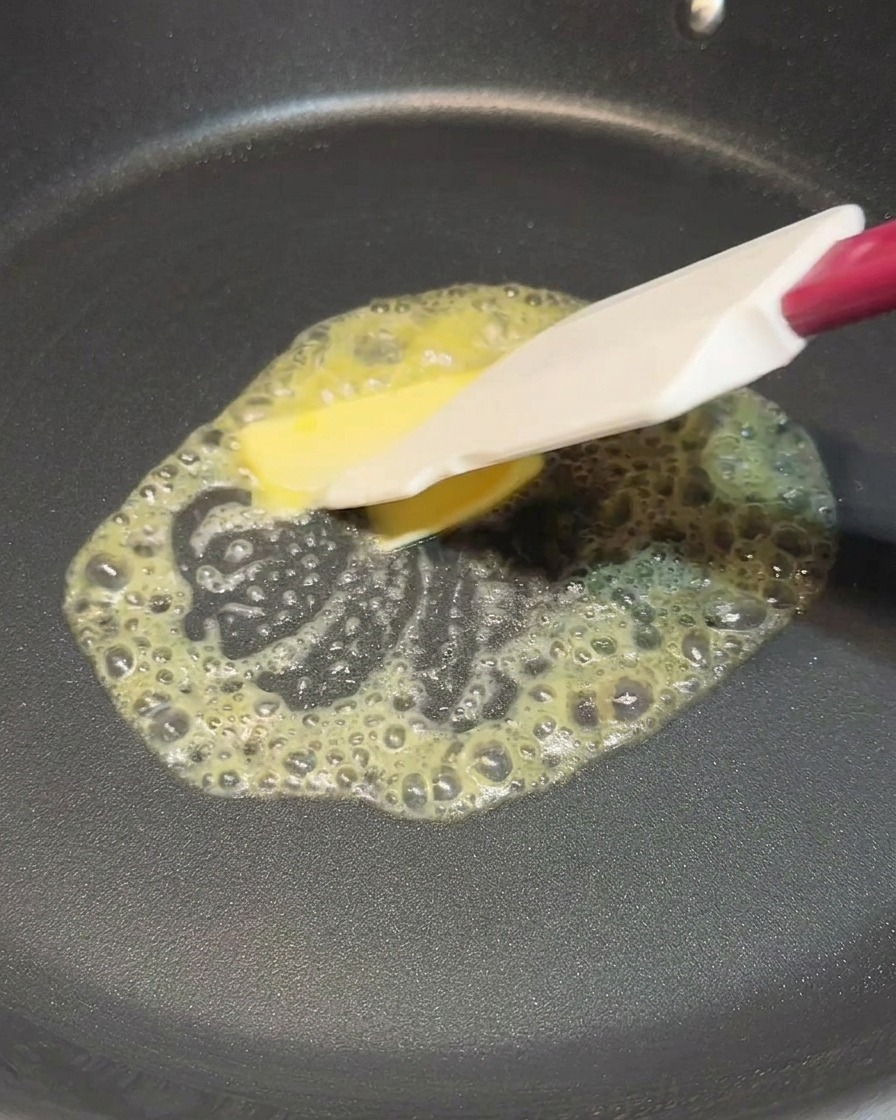 Une spatule étalant un carré de beurre en train de fondre dans une poêle noire fumante.