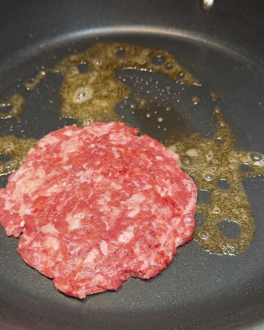 Un steak haché cru et persillé grésillant dans du beurre fondu au fond dune poêle noire.