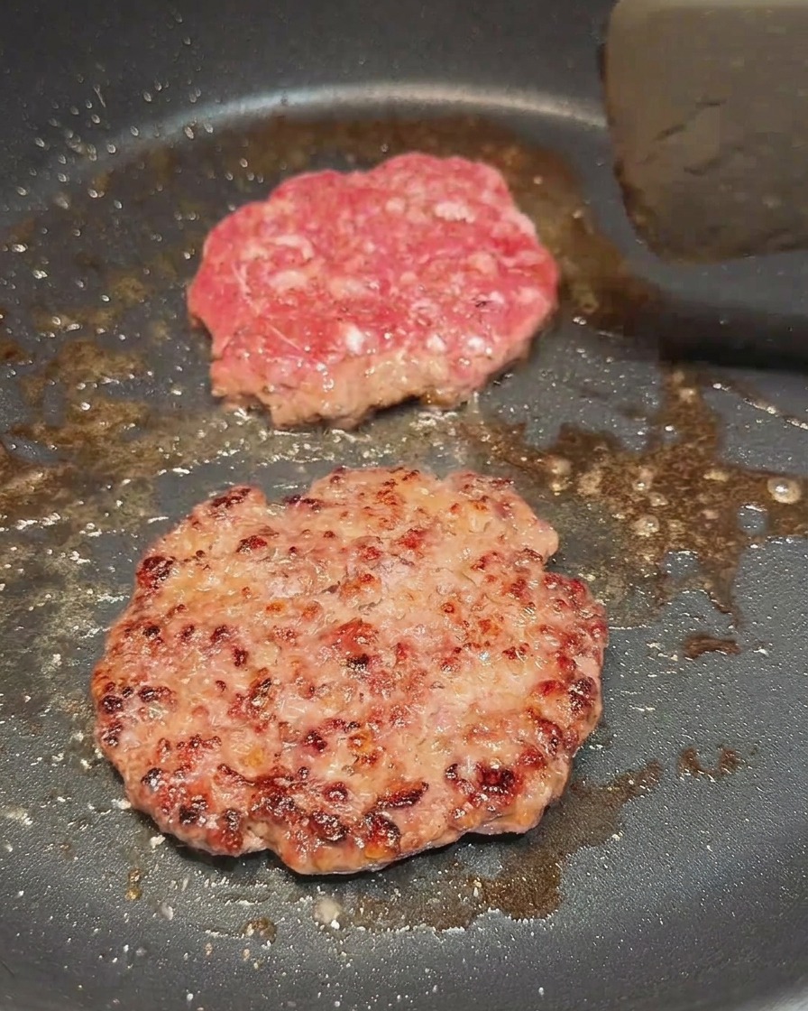 Deux steaks de bœuf cuisant dans une poêle, lun deux venant dêtre retourné pour dévoiler une face bien brunie.