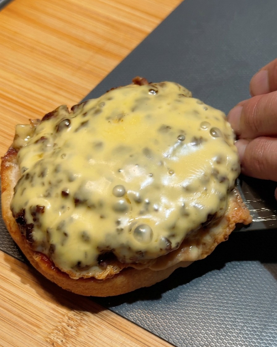 Une spatule transférant deux steaks hachés superposés, recouverts de fromage fondu, sur la base dun pain à burger.