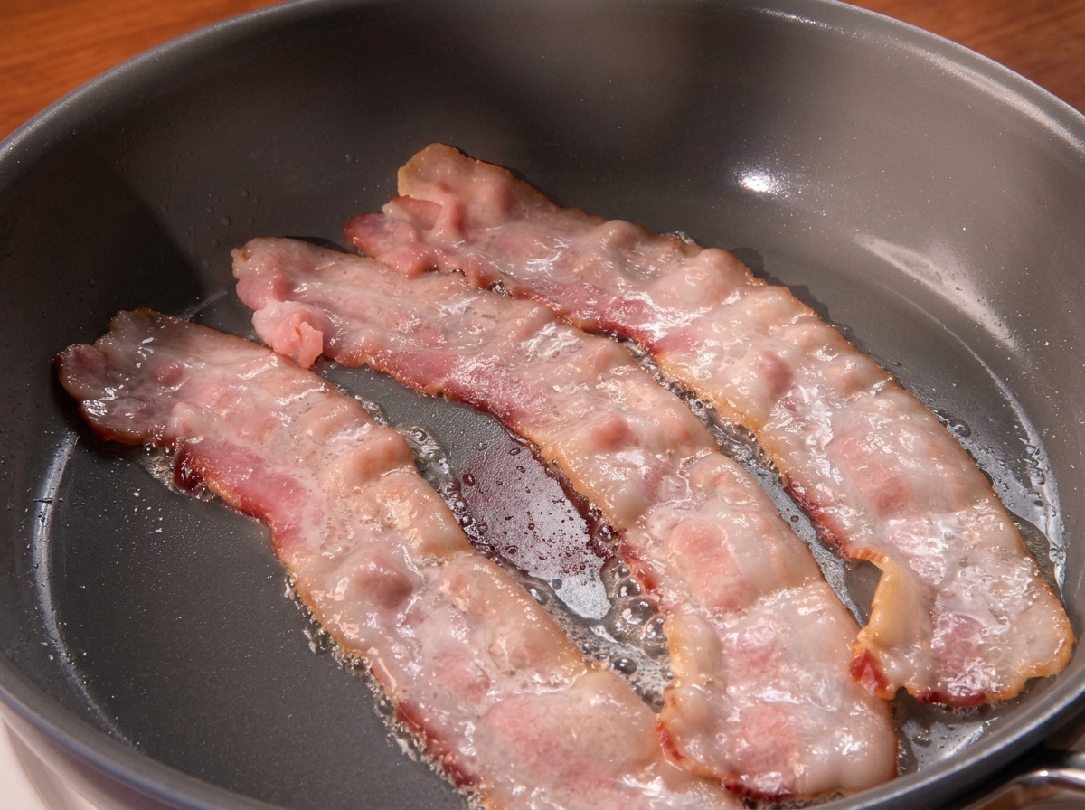 Trois tranches de bacon grésillant dans une poêle chaude.