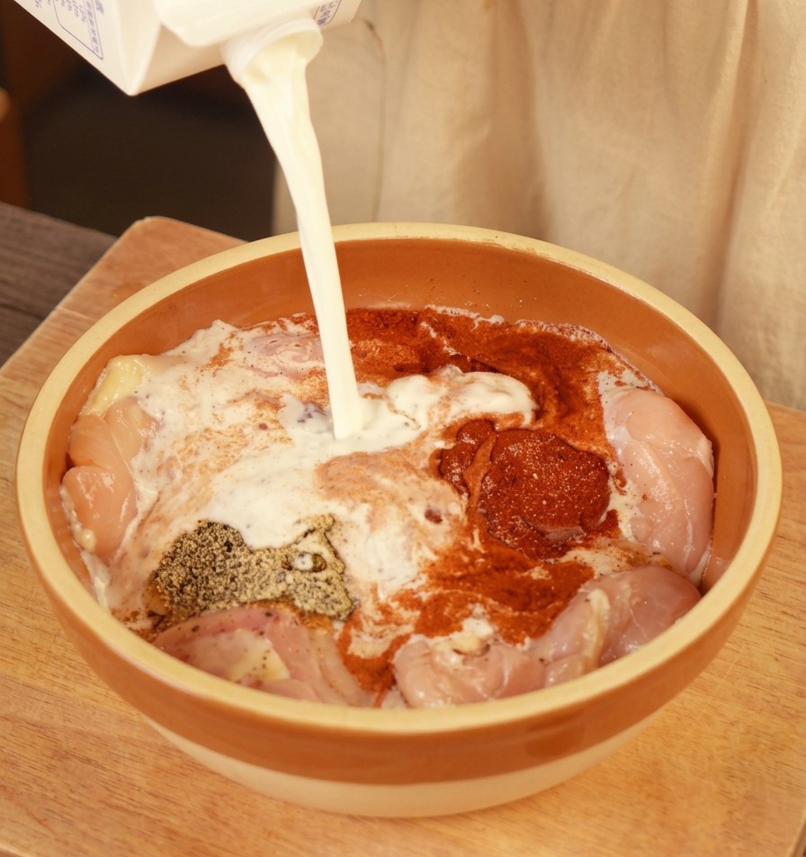 Lait frais versé dune brique dans un bol contenant les morceaux de poulet assaisonnés.