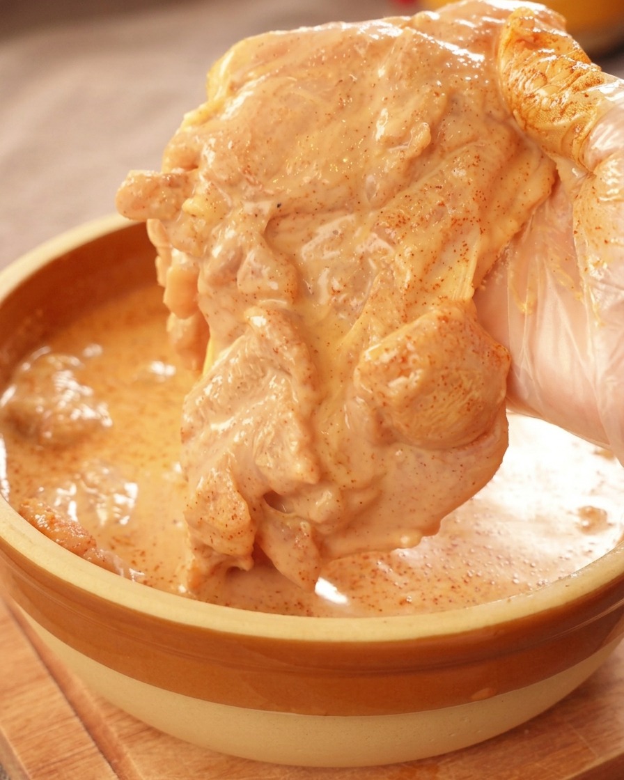 Une main gantée soulevant un morceau de poulet généreusement nappé dune marinade orange épaisse.