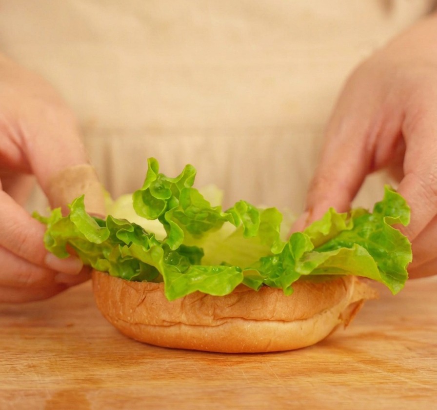 Mains déposant des feuilles de laitue sur la base dun pain à burger toasté.