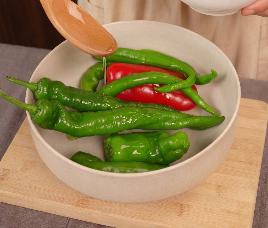 Huile de cuisson versée dune cuillère en bois sur un mélange de piments frais rouges et verts dans un bol clair.