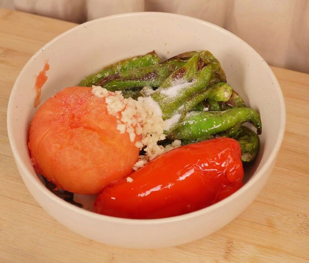 Un bol de piments rôtis et une tomate surmontés dail frais haché et dune pincée de sel avant le mélange.