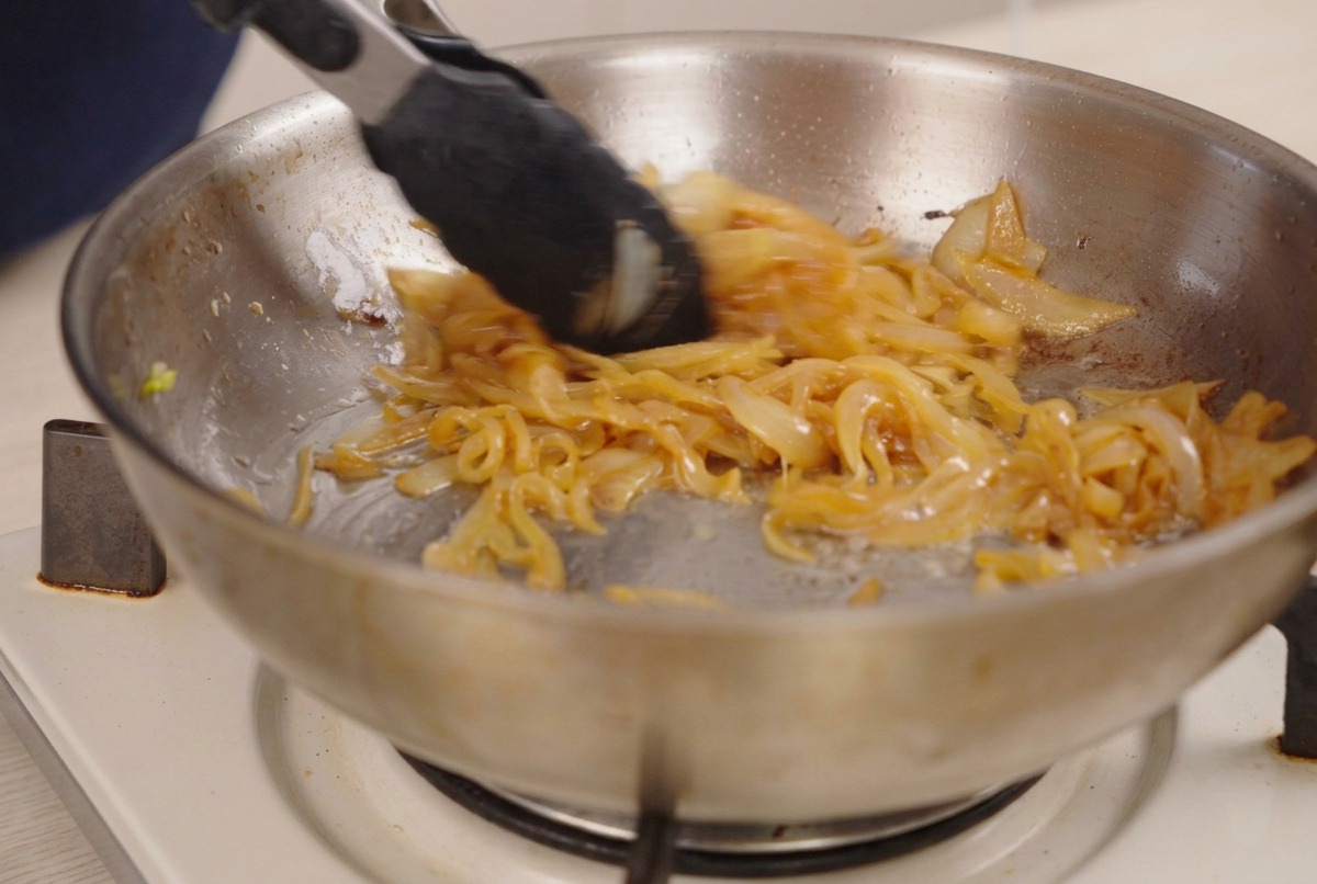 Une pince remuant des oignons très bruns et caramélisés dans une poêle.