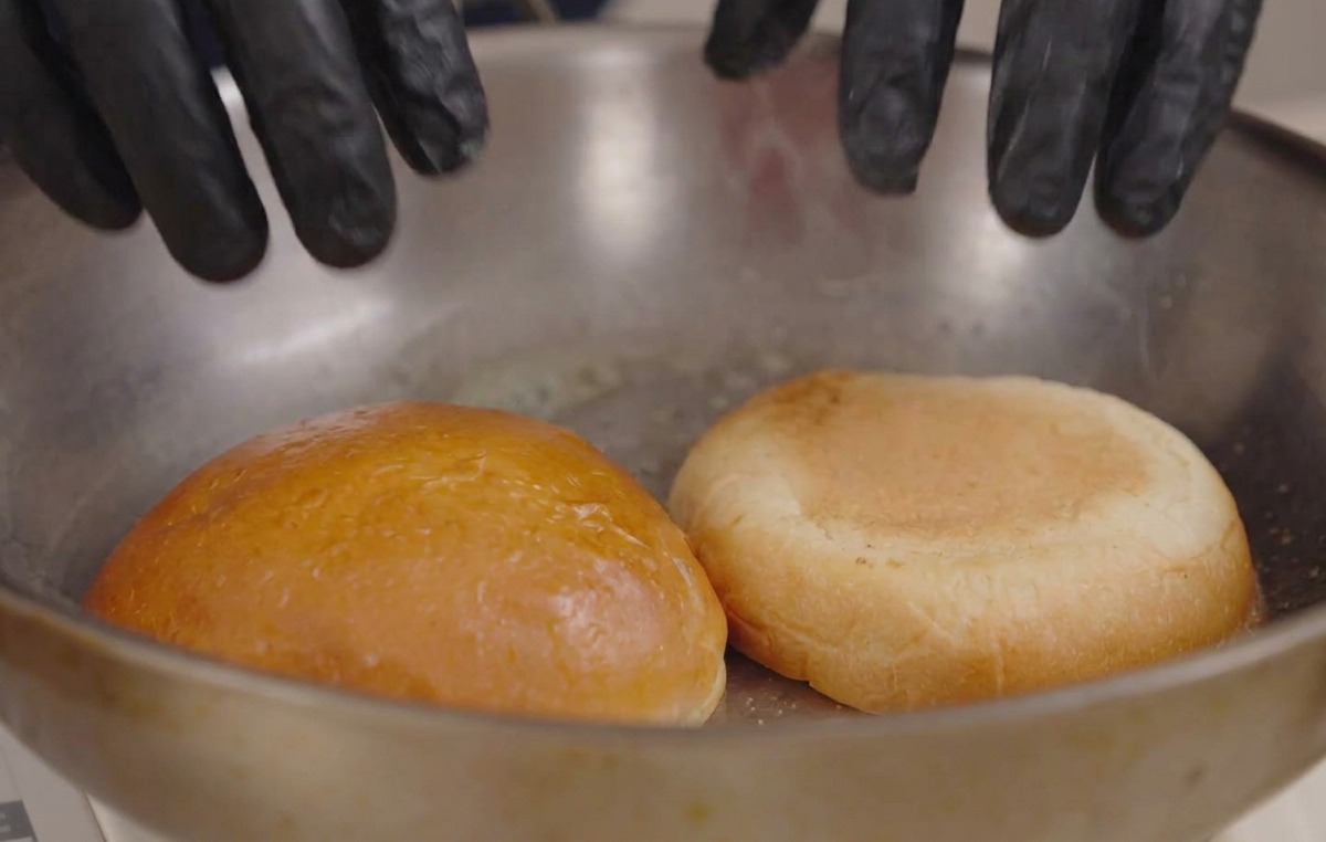 Mains pressant deux moitiés de pains à burger face contre terre dans une poêle avec du beurre fondu.