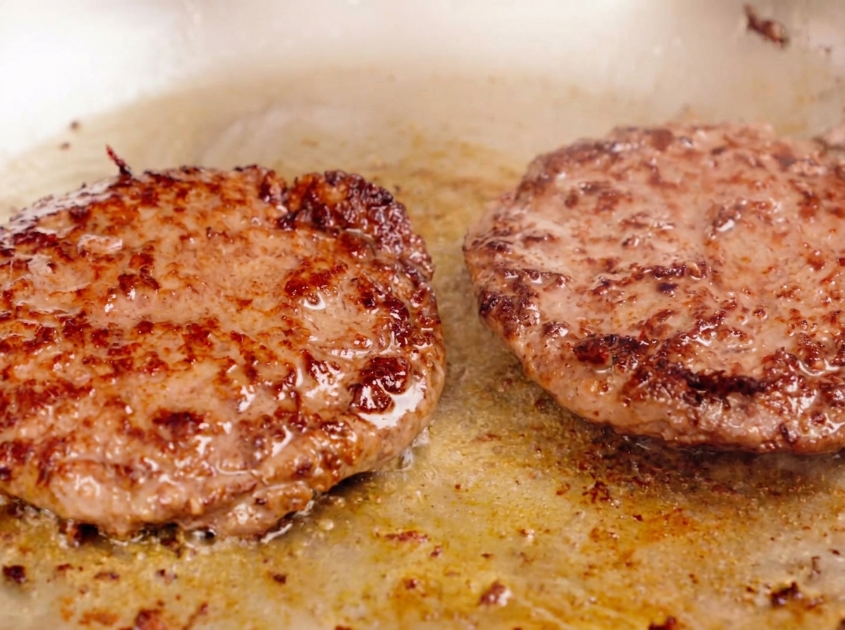 Deux steaks de bœuf épais grillant dans une poêle avec une croûte bien marquée.