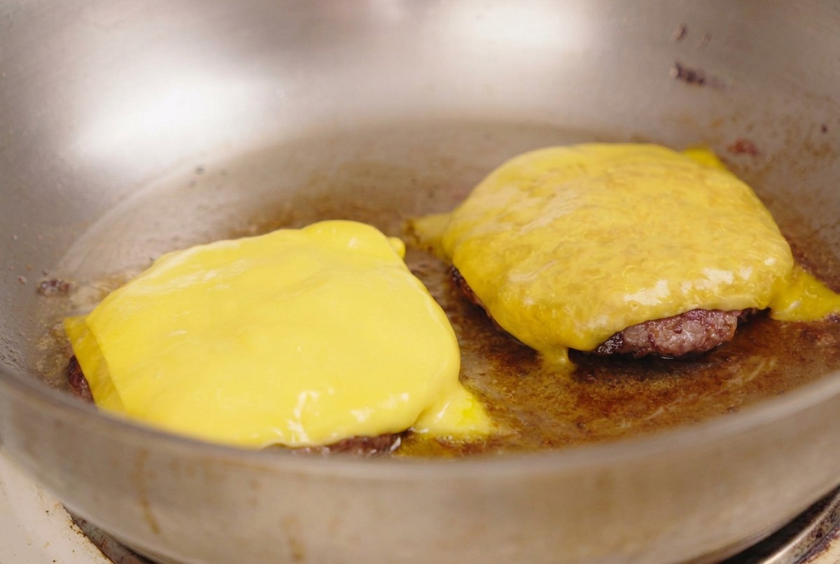 Tranches de fromage jaune fondant sur deux steaks de bœuf dans une poêle.