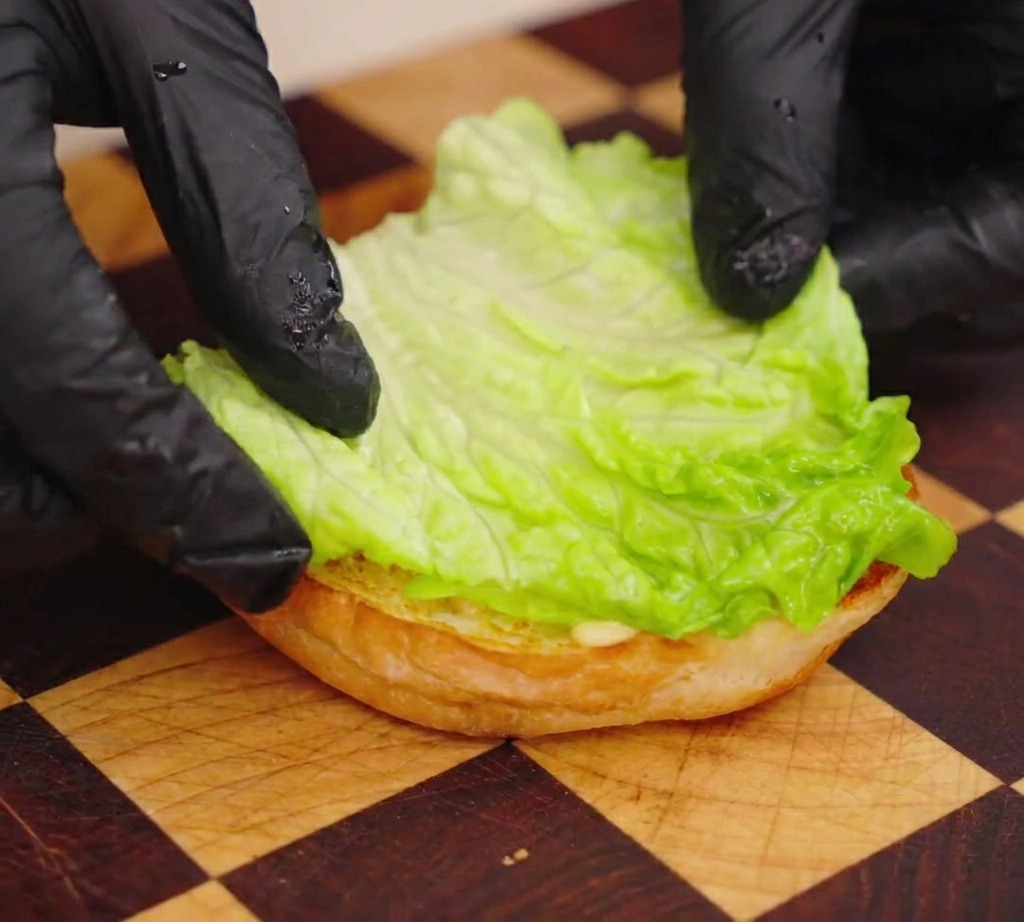 Une personne posant une feuille de laitue croquante sur la base dun pain à burger.
