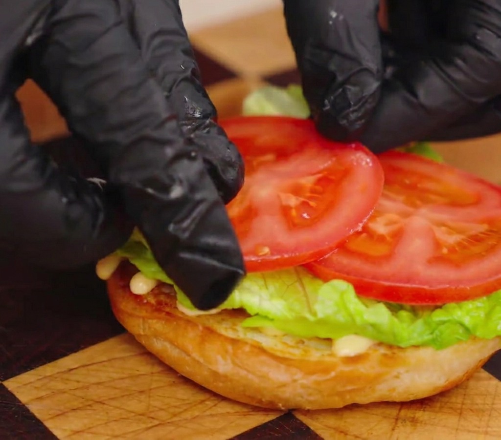 Gros plan sur des mains disposant deux tranches épaisses de tomate sur la salade.