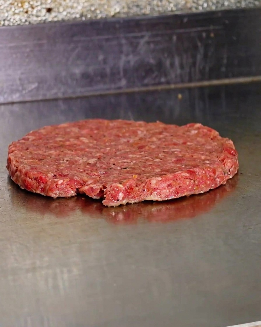 Un steak de bœuf cru fraîchement écrasé cuisant sur une plaque métallique chaude.