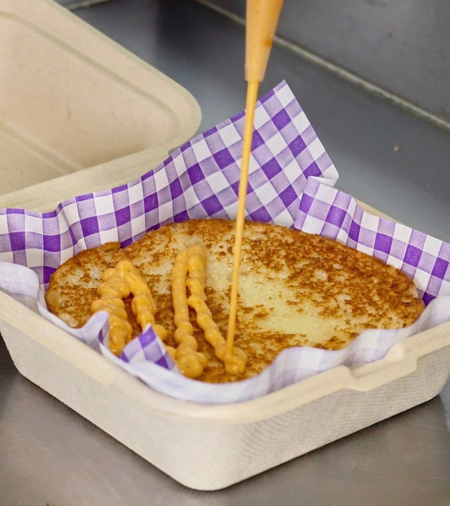 Un filet de sauce crémeuse orange versé sur le centre dun pain à burger toasté dans une boîte à emporter.