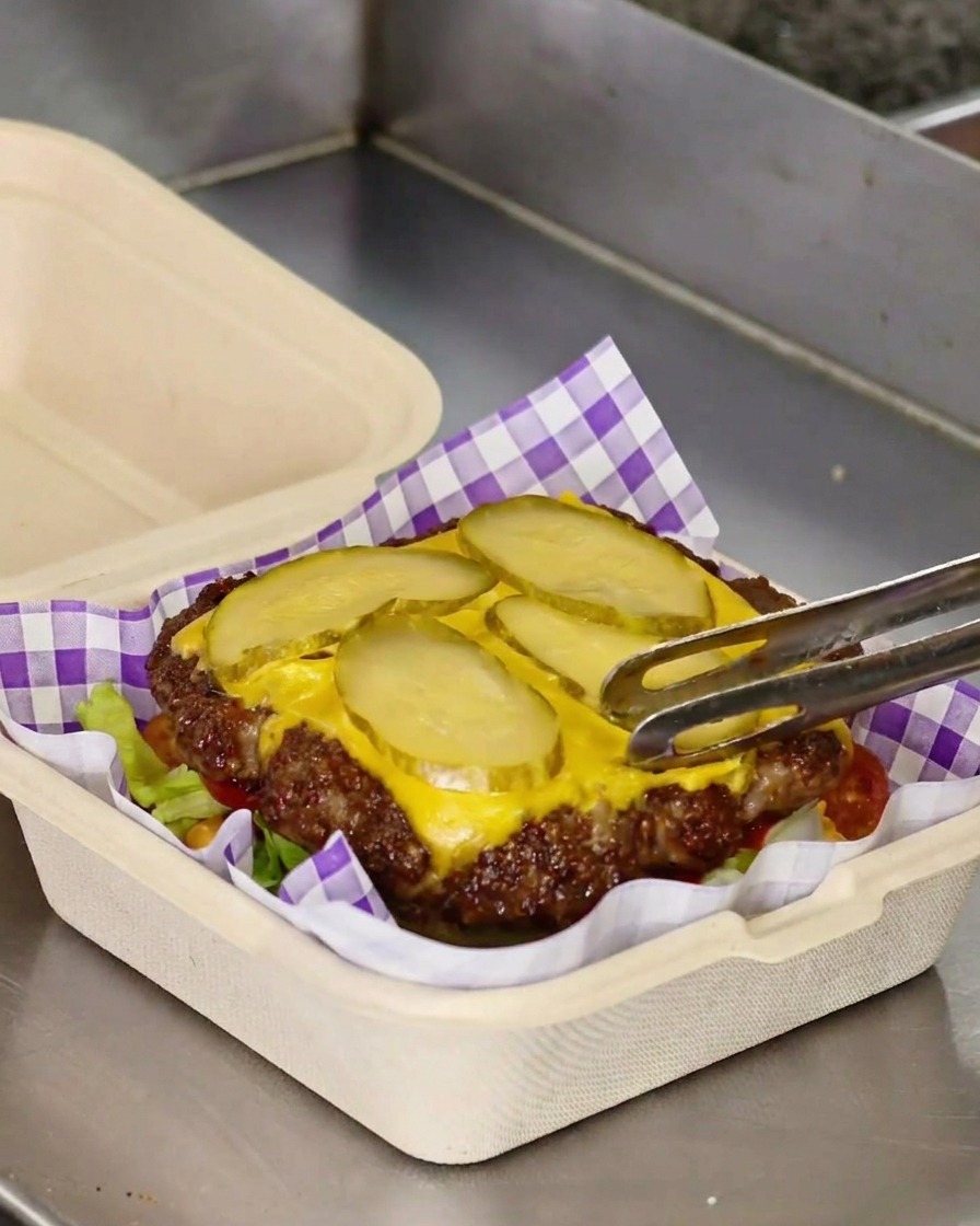 Transfert dun steak de smash burger avec fromage fondu et cornichons sur un lit de laitue.