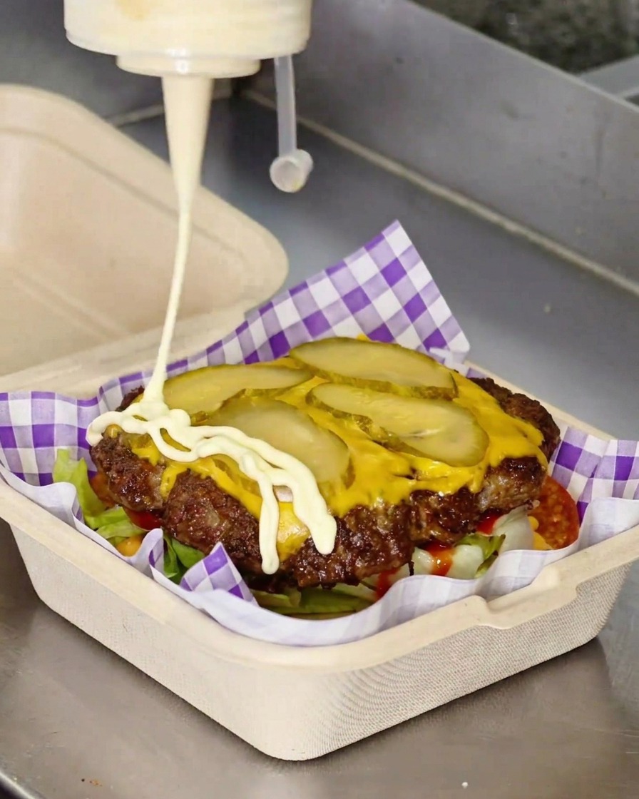 De la mayonnaise blanche versée en zigzag sur un steak de cheeseburger.