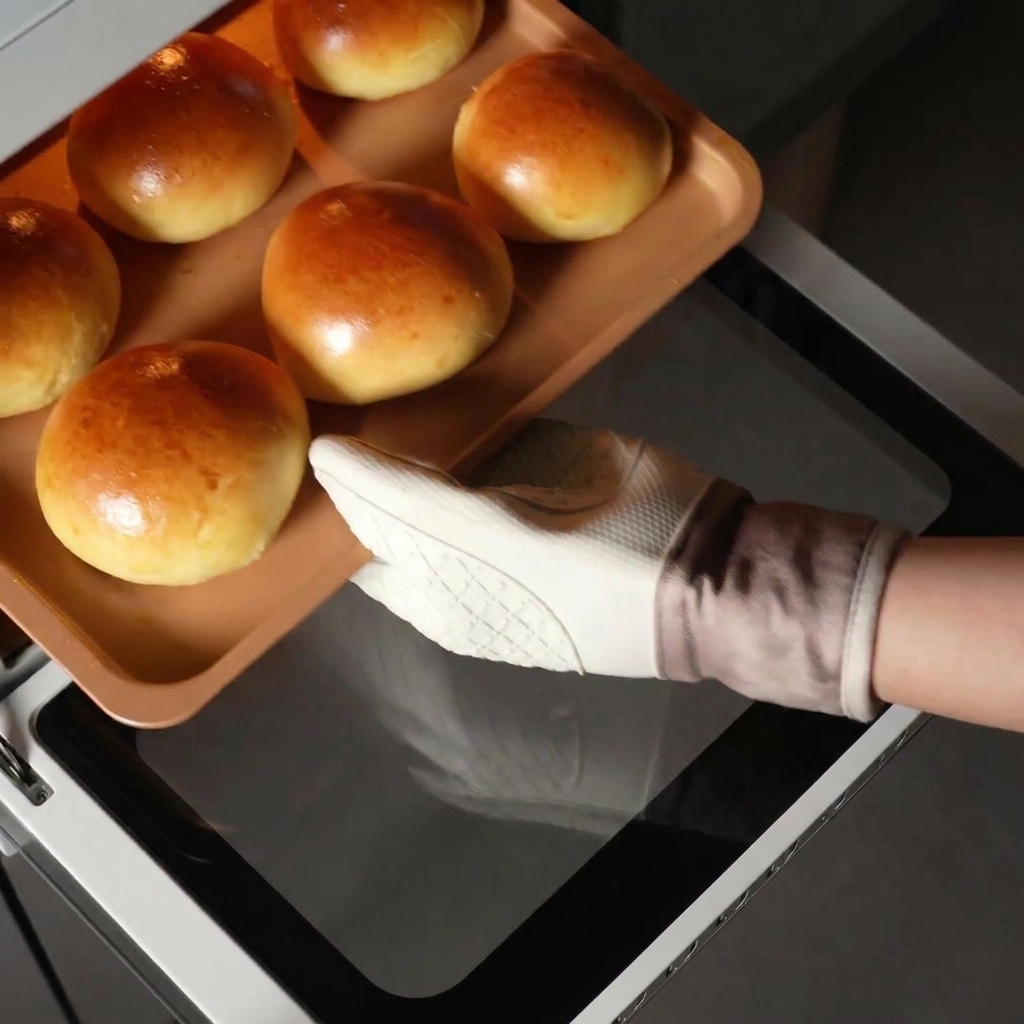 Une main sortant une plaque de cuisson remplie de buns briochés dorés dun four chaud.