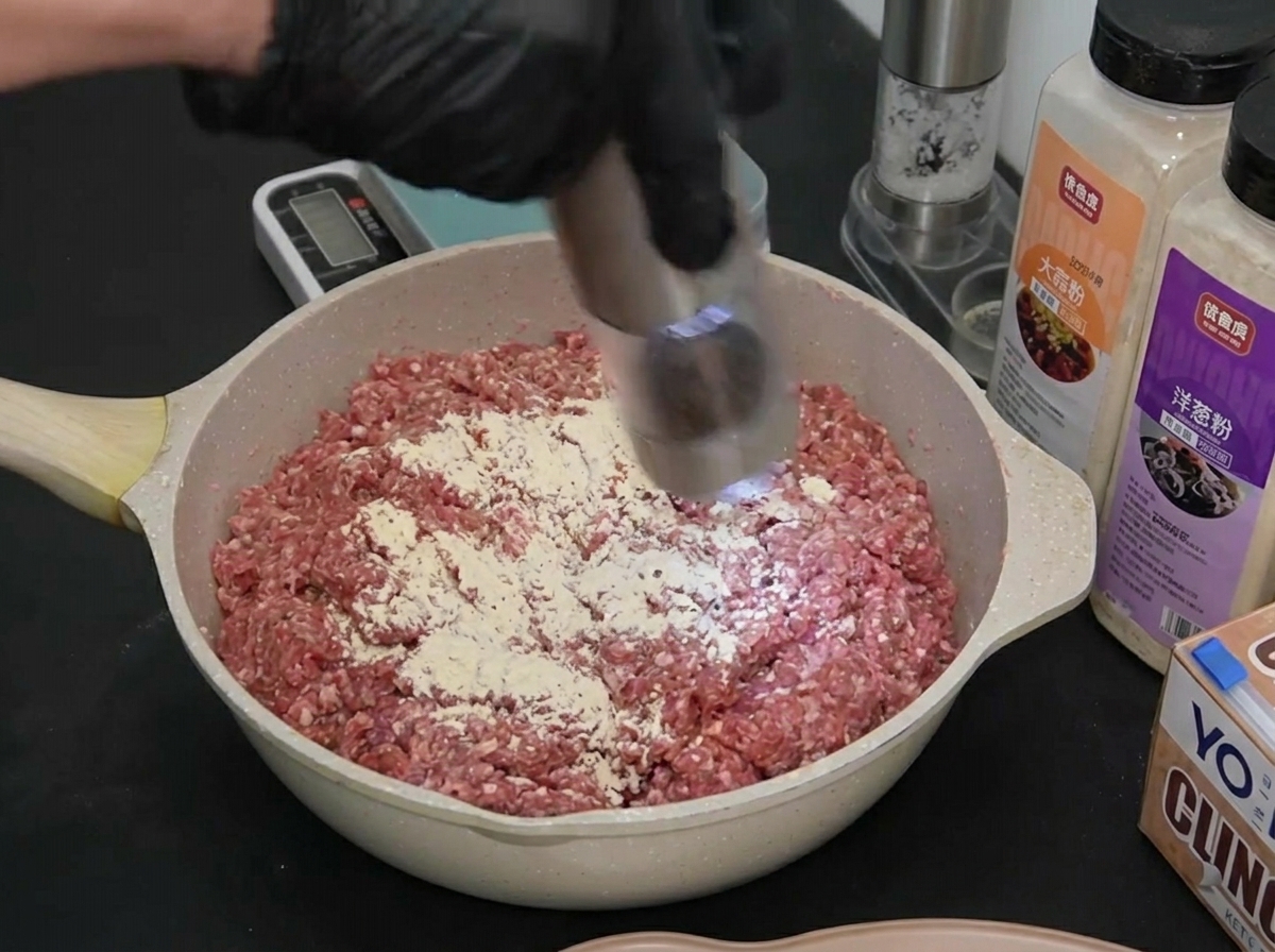 Une main utilisant un moulin électrique pour disperser du poivre noir sur la viande assaisonnée.