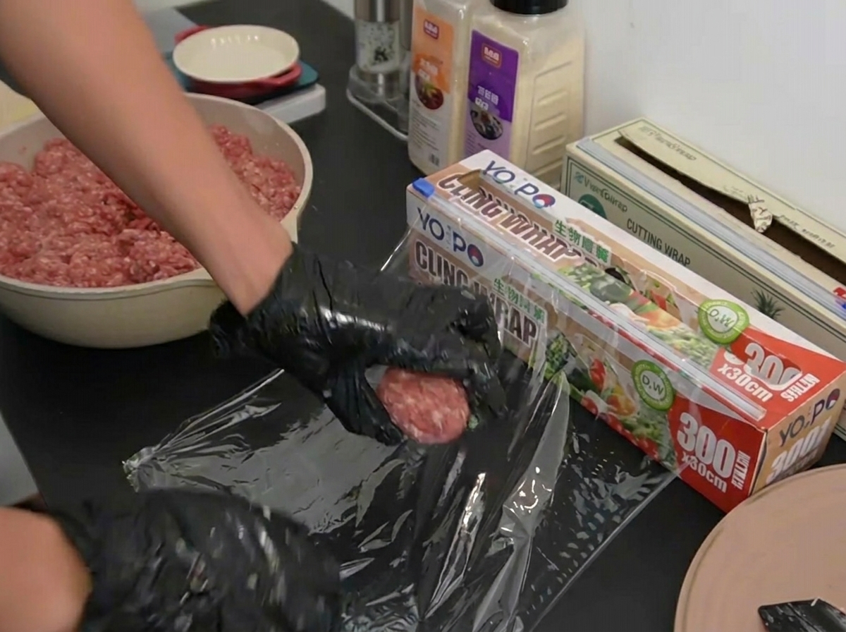 Mains gantées posant une boule de bœuf portionnée sur une feuille de film plastique.