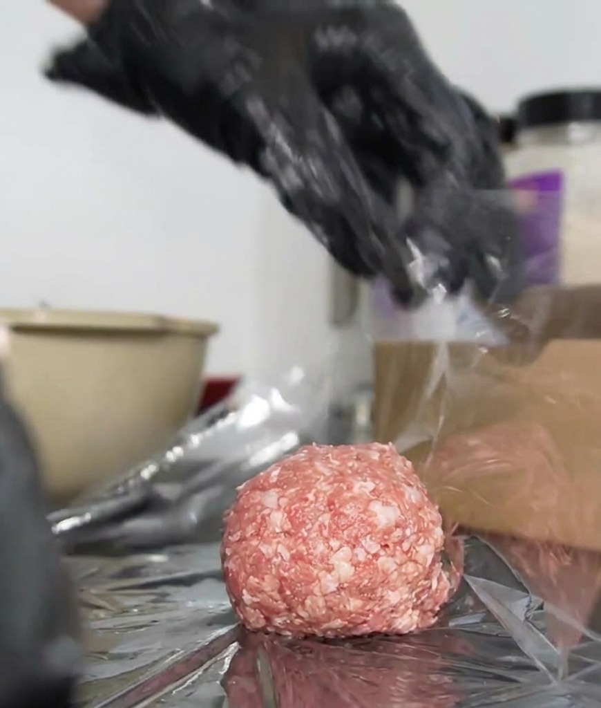 Mains gantées tordant fermement le film plastique autour dun steak de bœuf pour créer un emballage hermétique.