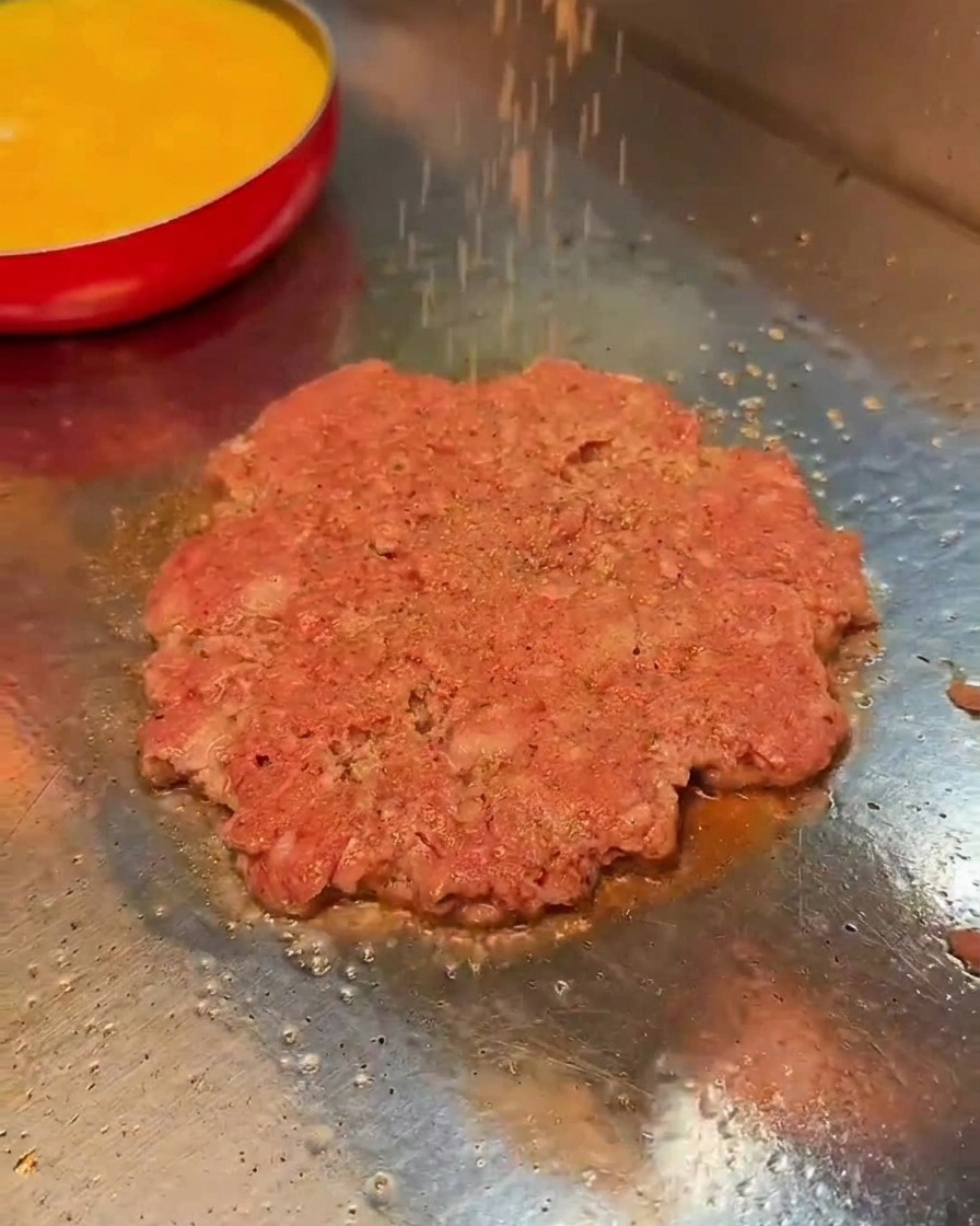 Sel et poivre noir saupoudrés sur un steak de bœuf en train de cuire.