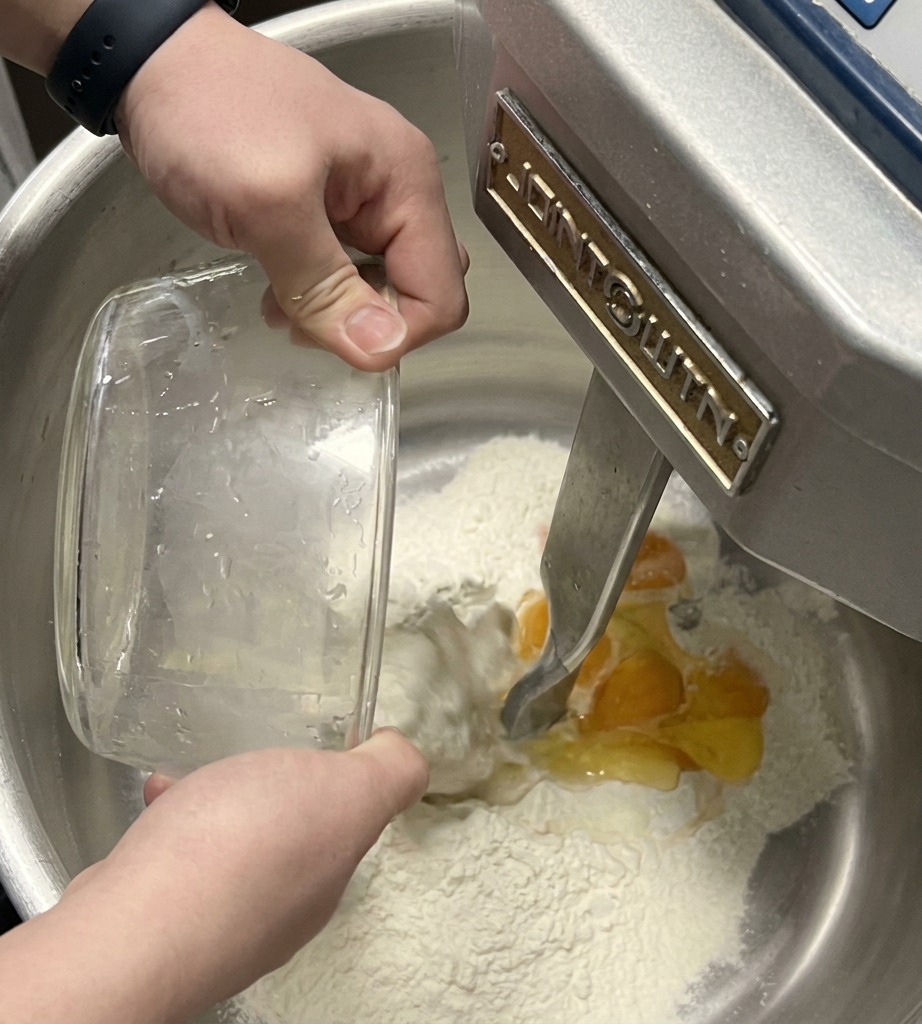 Crochet dun batteur sur socle incorporant les œufs et le liquide dans la farine dans un bol en inox.