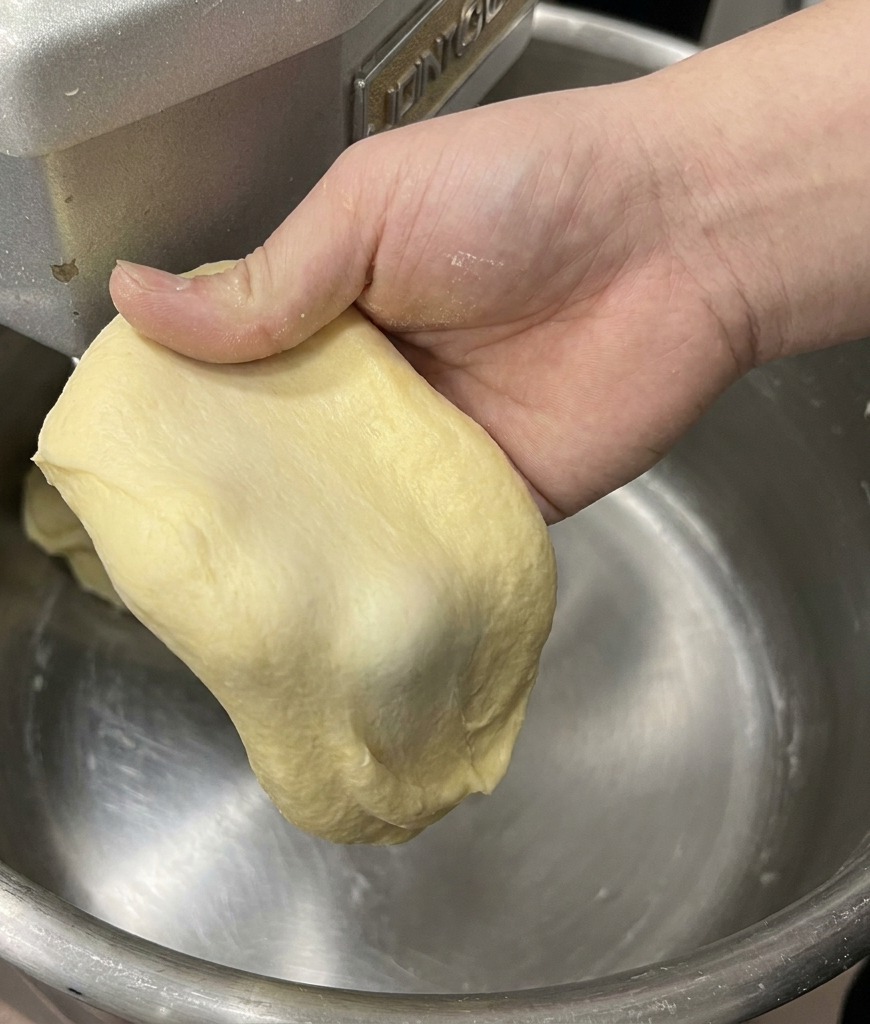 Une main étirant une pièce de pâte à brioche pour montrer la membrane fine et résistante du test de la fenêtre.