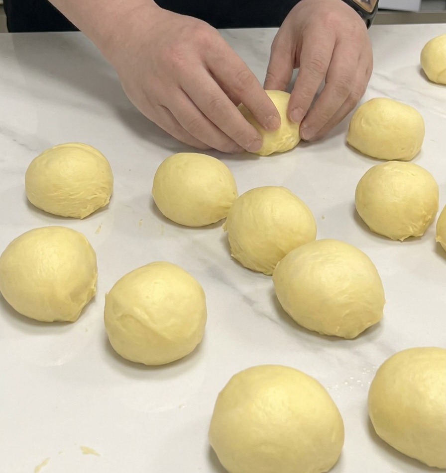 Mains façonnant de petites portions de pâte à brioche en boules sur un plan de travail en marbre blanc.