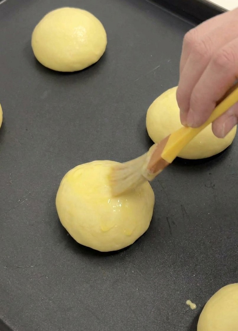 Un pinceau à pâtisserie appliquant une fine couche de dorure à lœuf sur le dessus dun pain brioché.