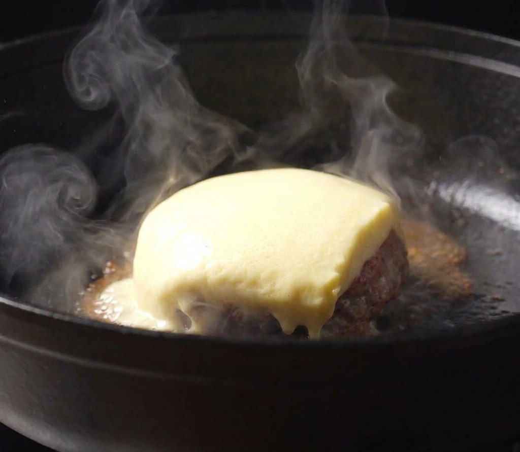 Une tranche de fromage fondant sur un steak avec de la sauce tomate dans une poêle en fonte.