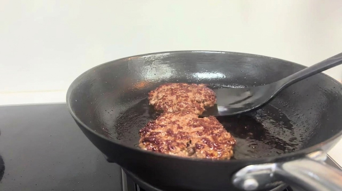 Une spatule noire retournant des steaks de bœuf bien dorés dans une poêle.